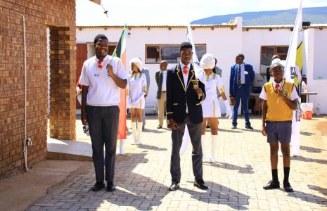 3 learners from BBKS High School holding the South African flag and flag with school emblem.