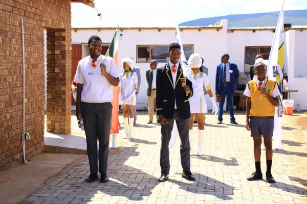 3 learners from BBKS High School holding the South African flag and flag with school emblem.